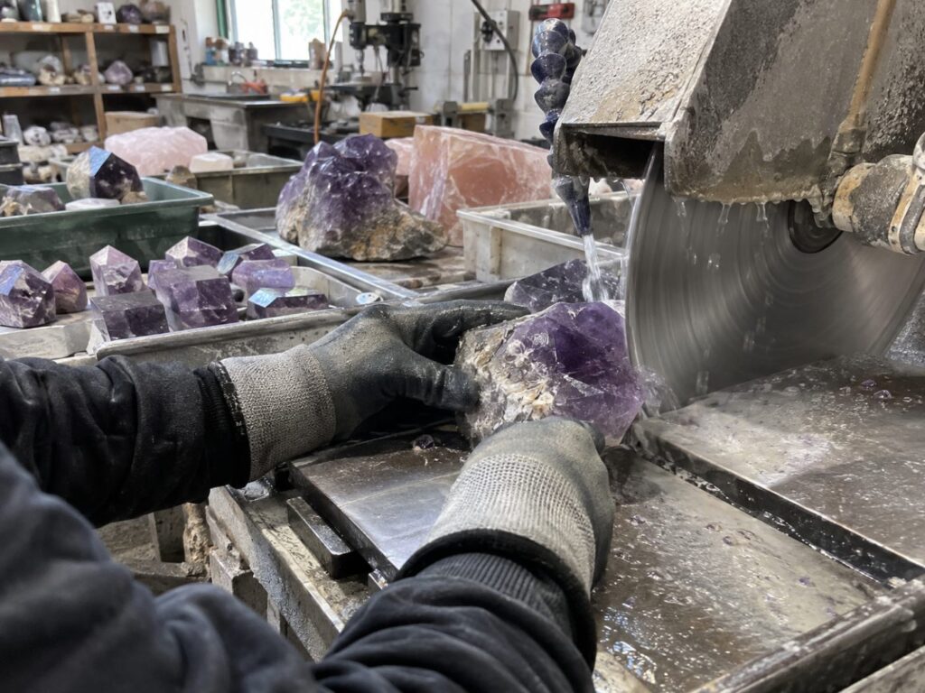 Crystal processing factory worker cutting a raw amethyst crystal with a wet saw